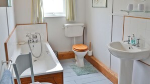 Un baño con bañera, inodoro, lavabo y una ventana con cortinas.