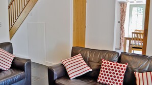 A living room with a brown leather sofa, two striped pillows, a wooden staircase, and a door leading to another room.