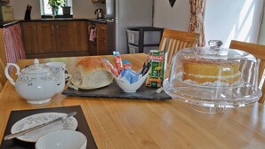 A table with a cake, tea bags, a teapot, and a bread roll.