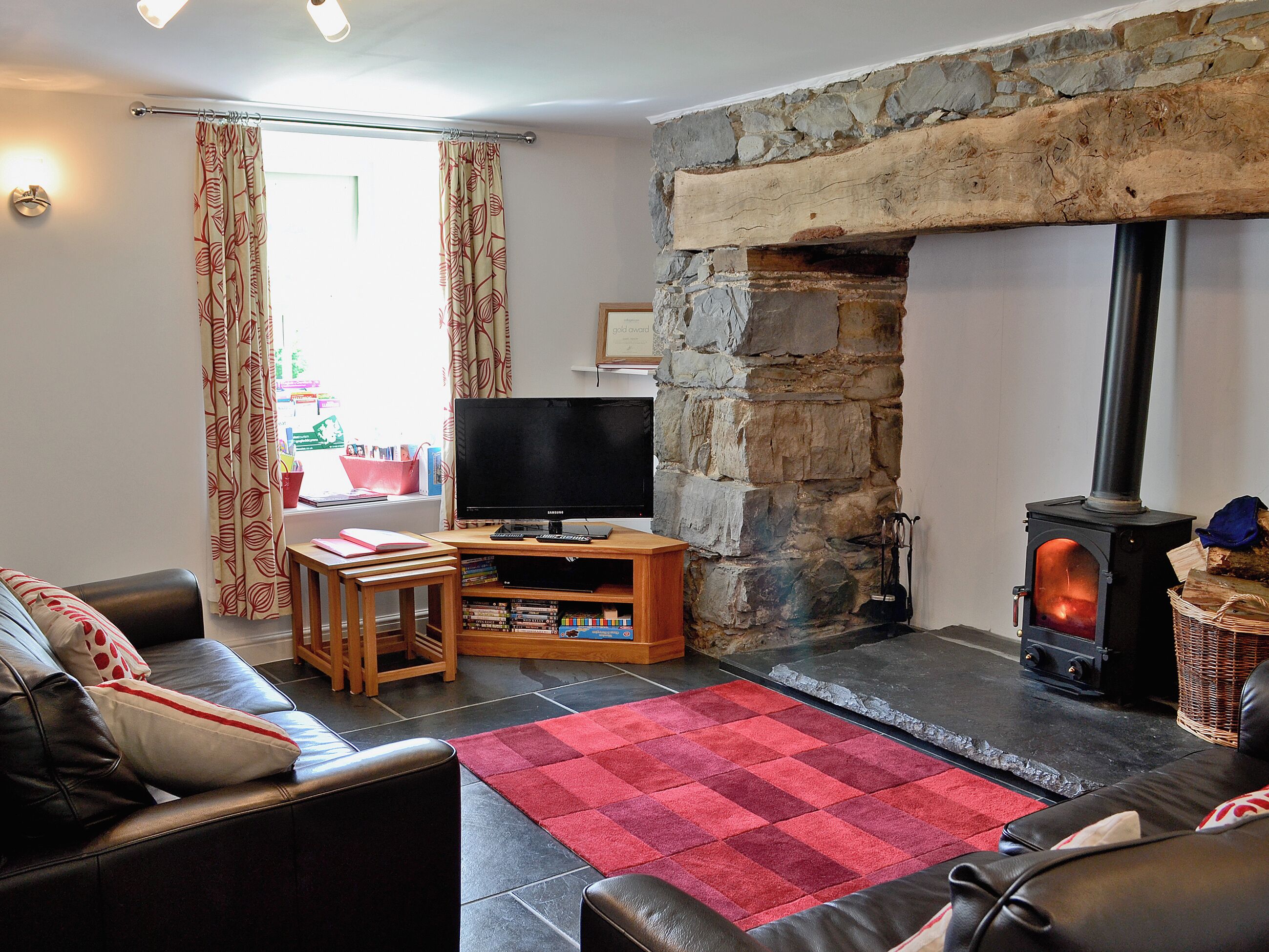 A living room with a stone fireplace, a television, a sofa, and a red rug.