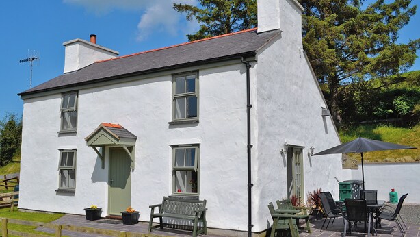 A white building with a grey roof, a green door, and a bench outside.