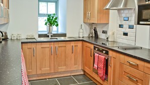 A modern kitchen with wooden cabinets, a stainless steel range hood, and a window with a plant.