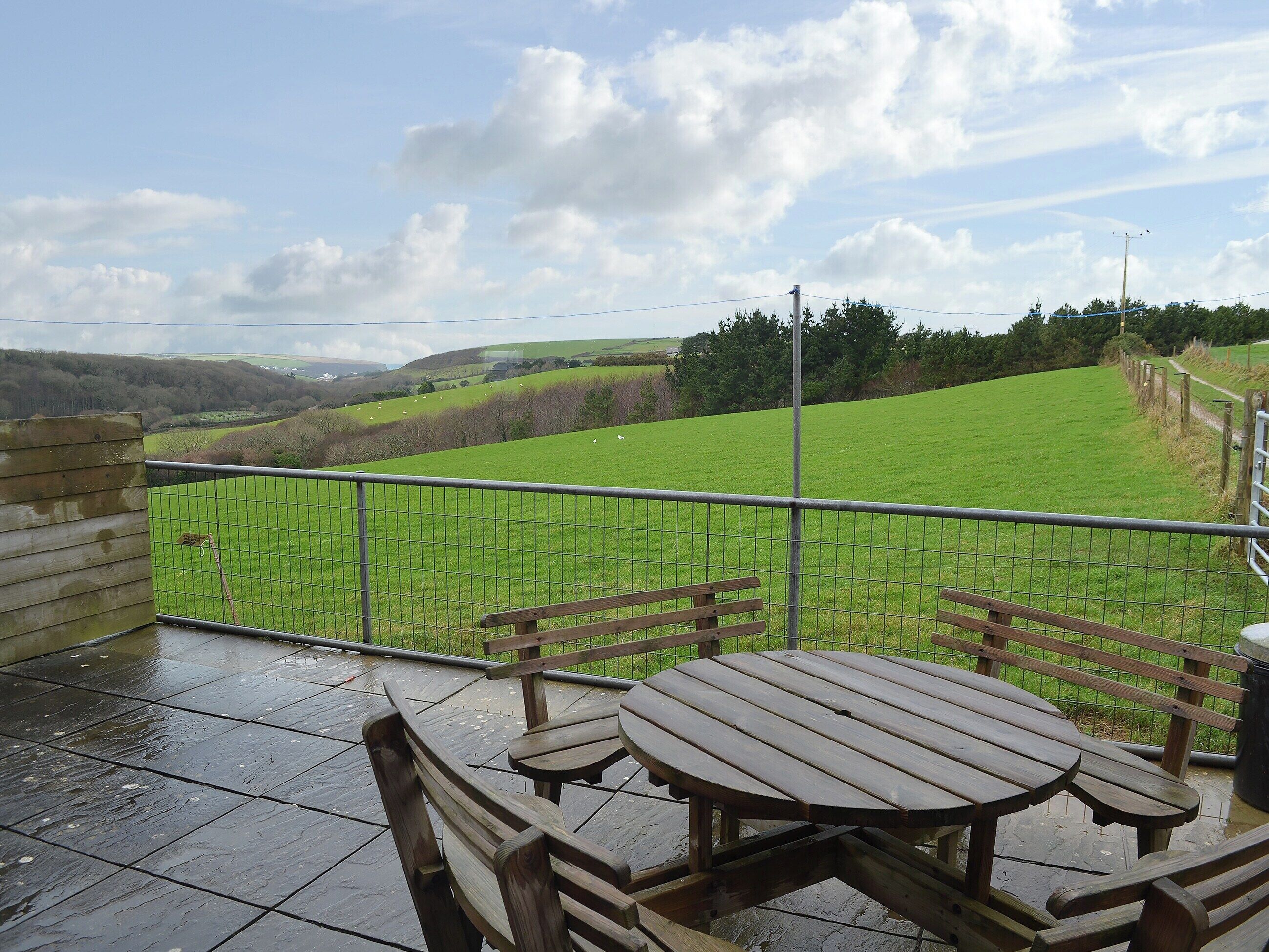 A patio with a table and benches overlooking a green field with sheep.