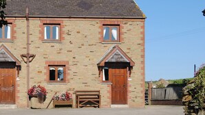 A two-story stone building with a traditional design, featuring a wooden bench outside and a metal pole in front. - 3 bedroom accommodation in St Mawgan, near Newquay (St Mawgan, near Newquay)