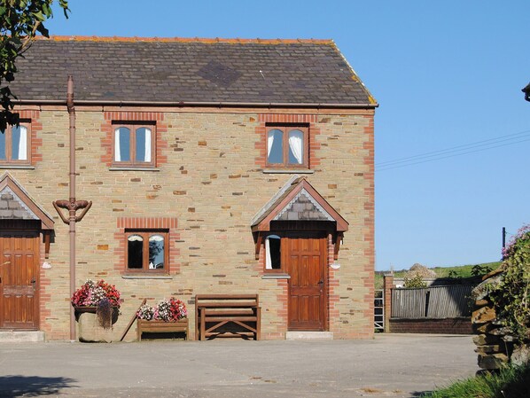 A two-story stone building with a traditional design, featuring a wooden bench outside and a metal pole in front. - 3 bedroom accommodation in St Mawgan, near Newquay (St Mawgan, near Newquay)