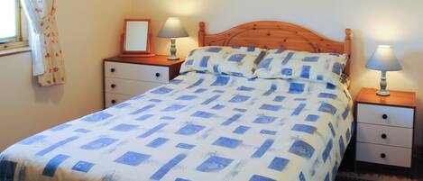 A bedroom with a bed, two bedside tables with lamps, a mirror, and a window with curtains.