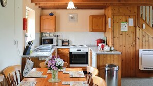 A cozy kitchen with wooden cabinets, a dining table set with placemats, and a trash can. - 3 bedroom accommodation in St Mawgan, near Newquay (St Mawgan, near Newquay)