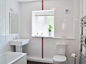 A bathroom with a white sink, a toilet, a window with a plant, and a mirror.