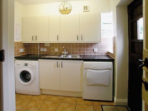A compact kitchen with a washing machine, dishwasher, and a clock on the wall.