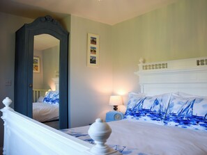 A bedroom with a bed, a nightstand, a lamp, a mirror, and a wall with framed pictures.
