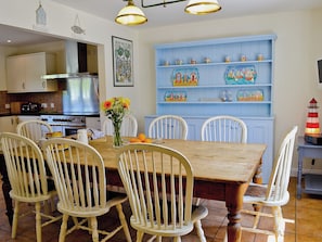 A dining area with a wooden table, white chairs, a vase with flowers, and a blue cabinet with decorative items.