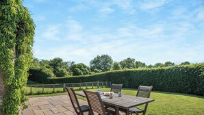 An outdoor patio with a wooden table and chairs, surrounded by a well-maintained hedge and a stone pathway. - 2 bedroom accommodation in Haytongate, near Brampton (Haytongate, near Brampton)