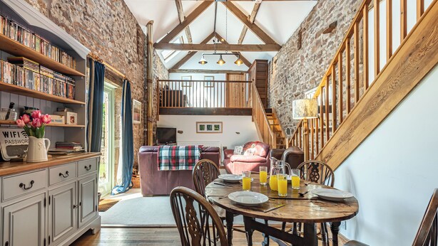 A rustic interior with exposed wooden beams, a stone wall, and a cozy seating area with a table set for breakfast. - 2 bedroom accommodation in Haytongate, near Brampton (Haytongate, near Brampton)