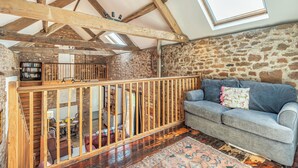 A rustic room with exposed wooden beams, a stone wall, a blue sofa, and a patterned rug. - 2 bedroom accommodation in Haytongate, near Brampton (Haytongate, near Brampton)