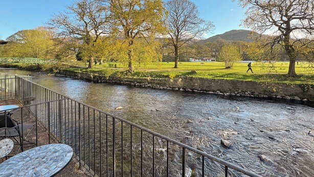 A riverside view with a stone wall, metal railing, and outdoor seating area. - 1 bedroom accommodation in Keswick (Keswick)