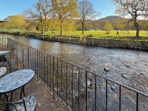 A riverside view with a stone wall, metal railing, and outdoor seating area. - 1 bedroom accommodation in Keswick (Keswick)