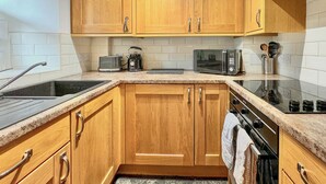 A kitchen with wooden cabinets, a microwave, a toaster, and a stove. - 1 bedroom accommodation in Keswick (Keswick)