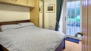 A bedroom with a bed, wooden cabinets, a window with curtains, and a door. - 1 bedroom accommodation in Keswick (Keswick)