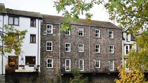 A stone building with multiple windows and a river in front. - 1 bedroom accommodation in Keswick (Keswick)