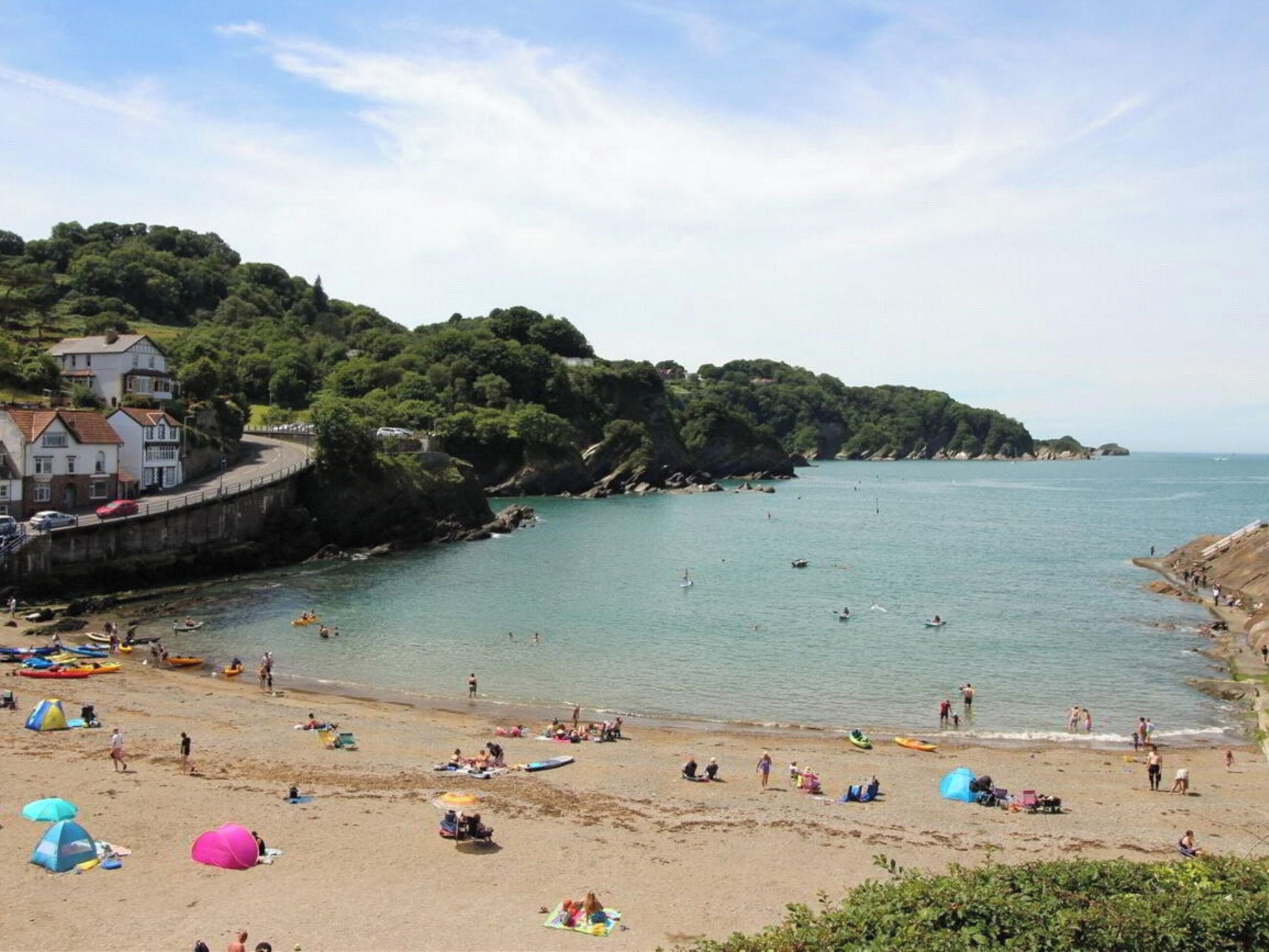 A beach with a rocky coastline, a few buildings, and people engaging in various activities.
