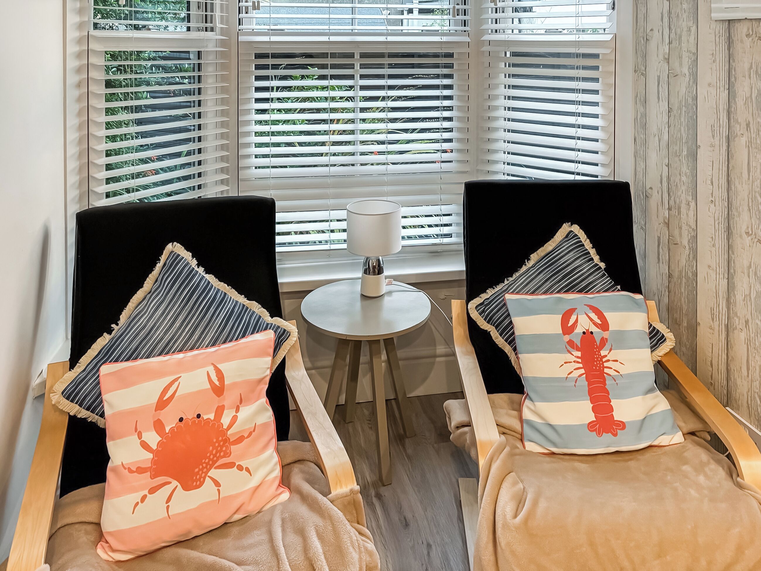 Two chairs with striped pillows, a small round table with a lamp, and a window with blinds.