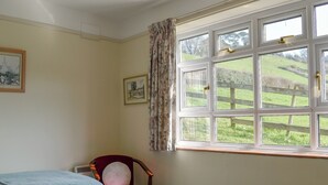 Une chambre avec deux lits, une chaise, une fenêtre donnant sur la campagne et deux tableaux encadrés accrochés au mur.