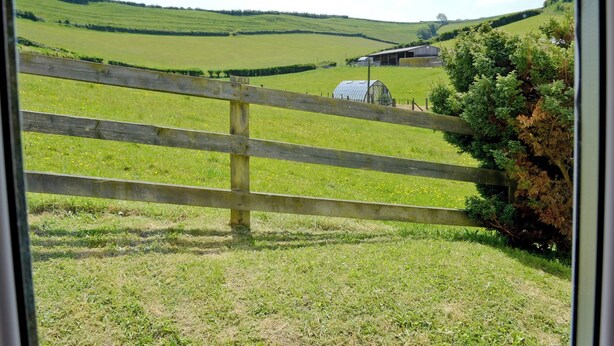 Un paysage rural avec des collines verdoyantes, une clôture en bois et une serre.
