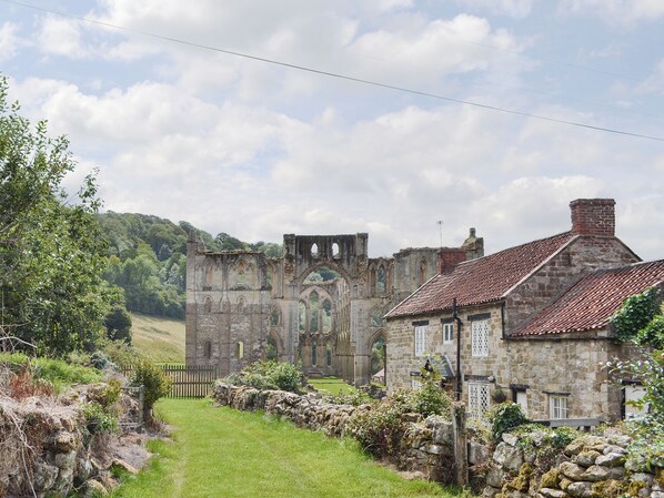 A historic stone building with a large arched entrance, a stone wall, and a grassy area. - Ashberry Farm Cottage (Rievaulx near Helmsley)