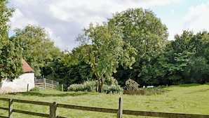 Een landelijk landschap met een houten hek, een wit gebouw met een rood dak en dichte groene bomen.