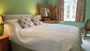 Een slaapkamer met een groot bed, een kapstok, een spiegel en een raam met gordijnen.