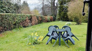 A garden with a table and chairs, surrounded by a hedge and trees. - Enchanted by thatch and character. (Catfield, near Potter Heigham)