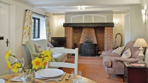 A living room with a fireplace, a sofa, a dining table with a vase of flowers, and a television. - Enchanted by thatch and character. (Catfield, near Potter Heigham)