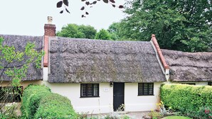 A traditional thatched-roof cottage with a white exterior, a black door, and a small garden with a pathway leading to the entrance. - Enchanted by thatch and character. (Catfield, near Potter Heigham)