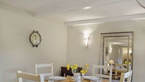 A dining room with a wooden table set for four, white chairs, a wall clock, a mirror, and a vase with flowers. - Enchanted by thatch and character. (Catfield, near Potter Heigham)