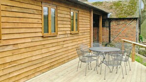 A wooden house with a brick extension, a patio with metal chairs and a table, and a chimney.