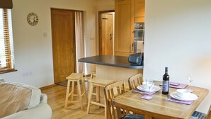 A cozy dining area with wooden furniture, a kitchen in the background, and a clock on the wall.