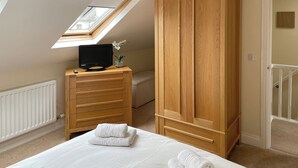 A bedroom with a sloped ceiling, a wooden wardrobe, a bed with white linens, a small TV on a wooden dresser, and a skylight. - 2 bedroom accommodation in Keswick (Keswick)