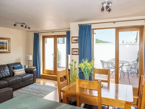 A living room with a sofa, a dining table with chairs, a TV, and a view of the outdoors. - 2 bedroom accommodation in Keswick (Keswick)