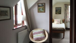 Ein Zimmer mit Korbmöbelstuhl, Bett, Heizkörper und einem Vorhangfenster.