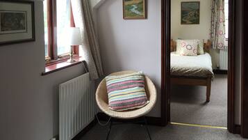 A room with a wicker chair, a bed, a radiator, and a window with curtains.