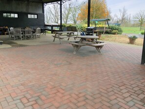 An outdoor patio area with brick flooring, picnic tables, and a barbecue grill.