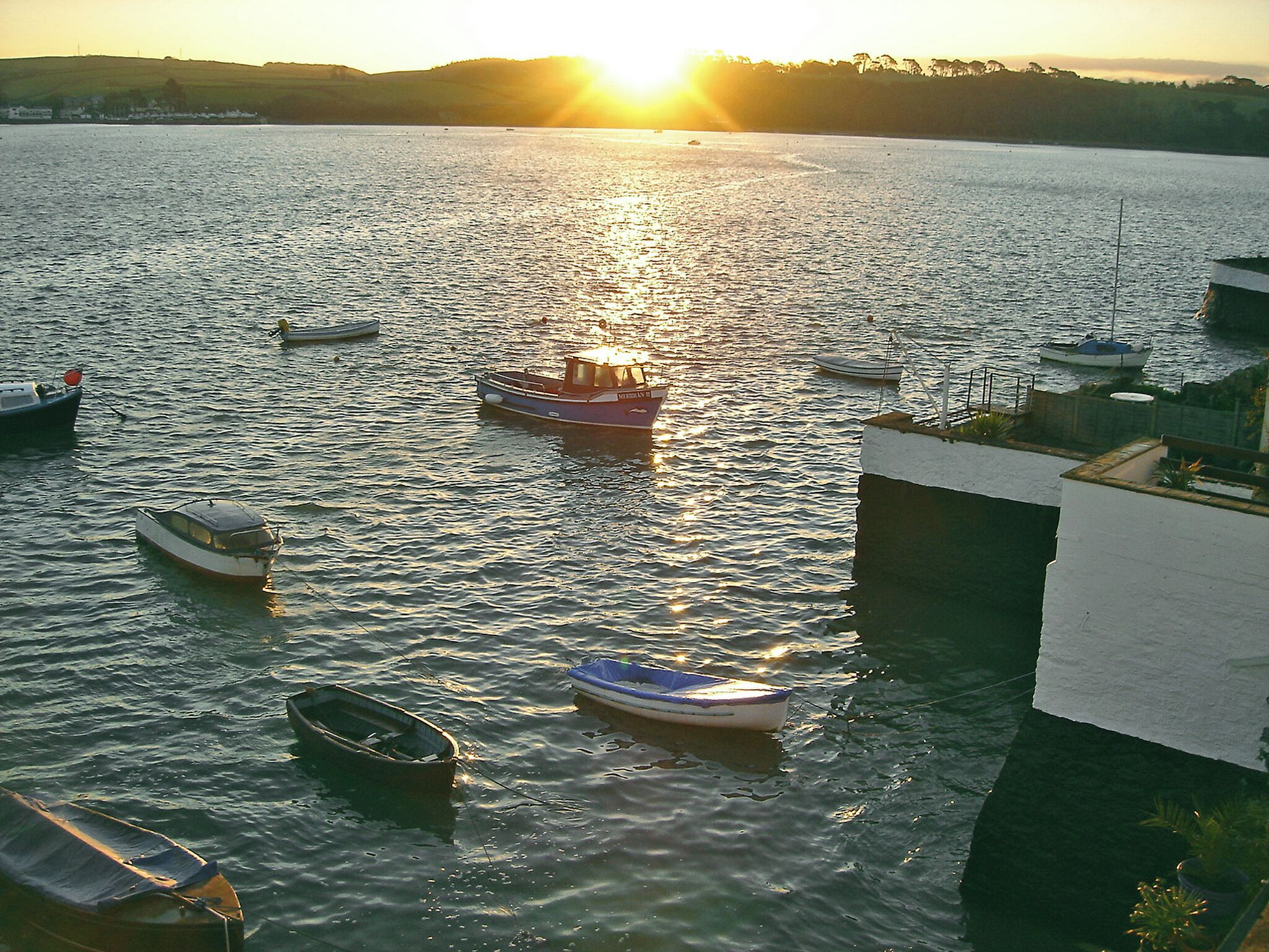 A marina with several boats docked, a building with a white exterior, and a sunset in the background.