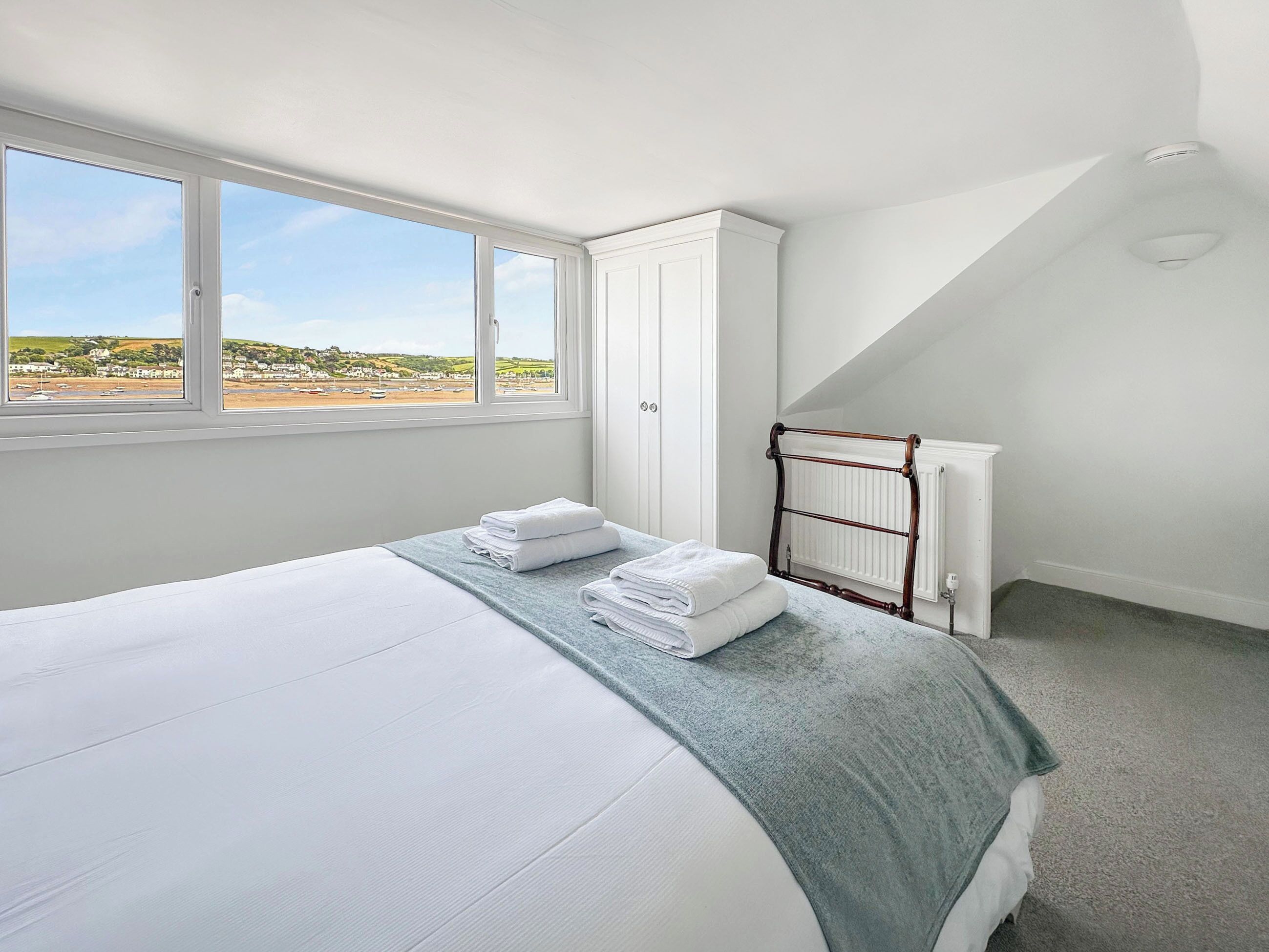 A bedroom with a bed, a window with a view, a radiator, and a towel rack.