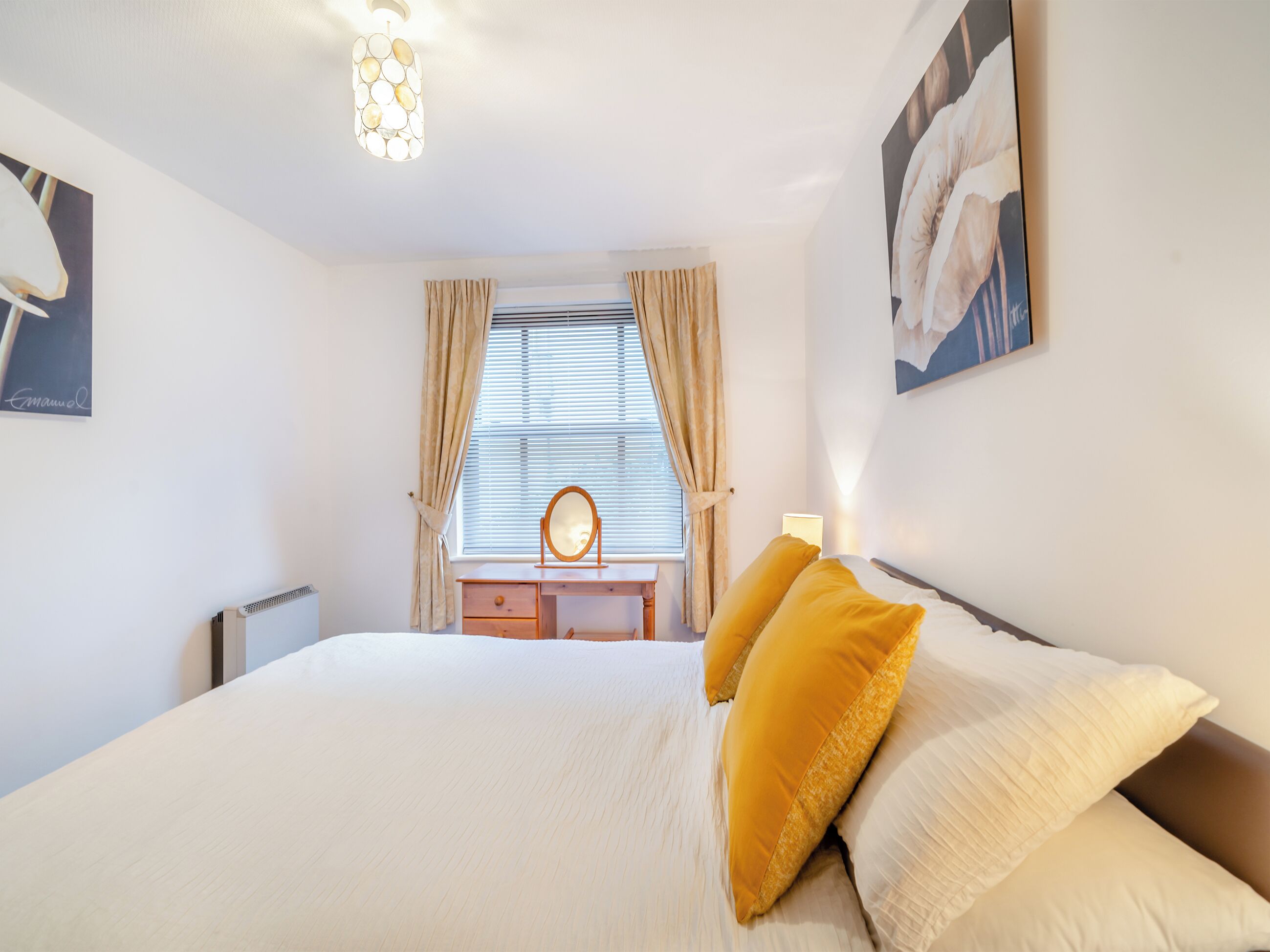 Une chambre à coucher avec un lit, une table de chevet, un miroir et une fenêtre avec des rideaux.