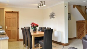 Un comedor con mesa de madera, sillas negras, una planta en maceta, luces empotradas en el techo y una escalera.