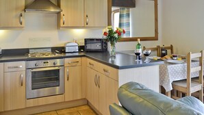 Una cocina con armarios de madera, horno empotrado, tostadora y una zona de comedor con mesa y sillas.