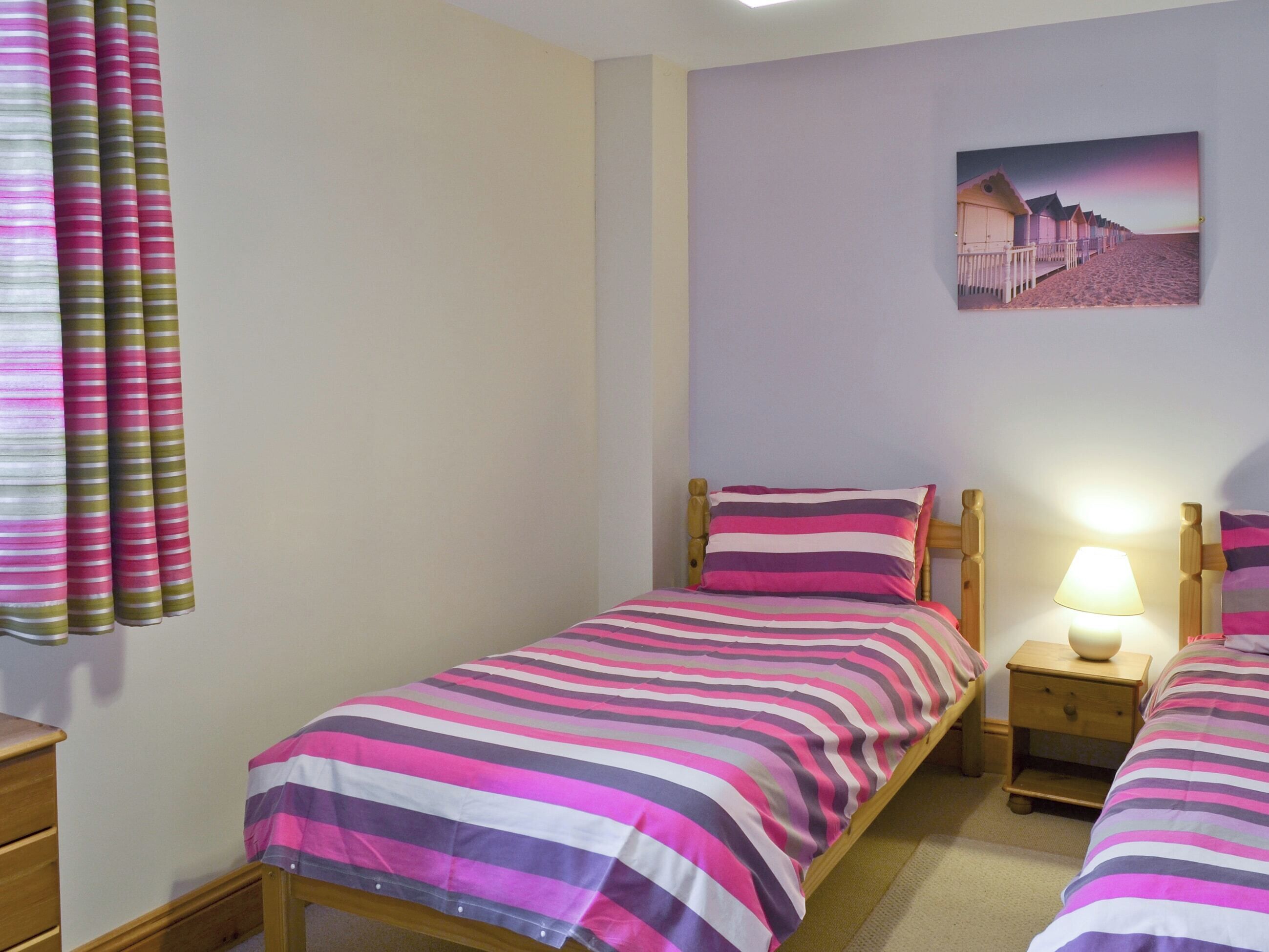 A bedroom with two single beds, a nightstand with a lamp, a wooden dresser, and a painting on the wall.