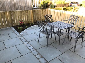 An outdoor patio with a stone floor, metal table and chairs, and a wooden fence. - 3 Catherine Cottages (Keswick)