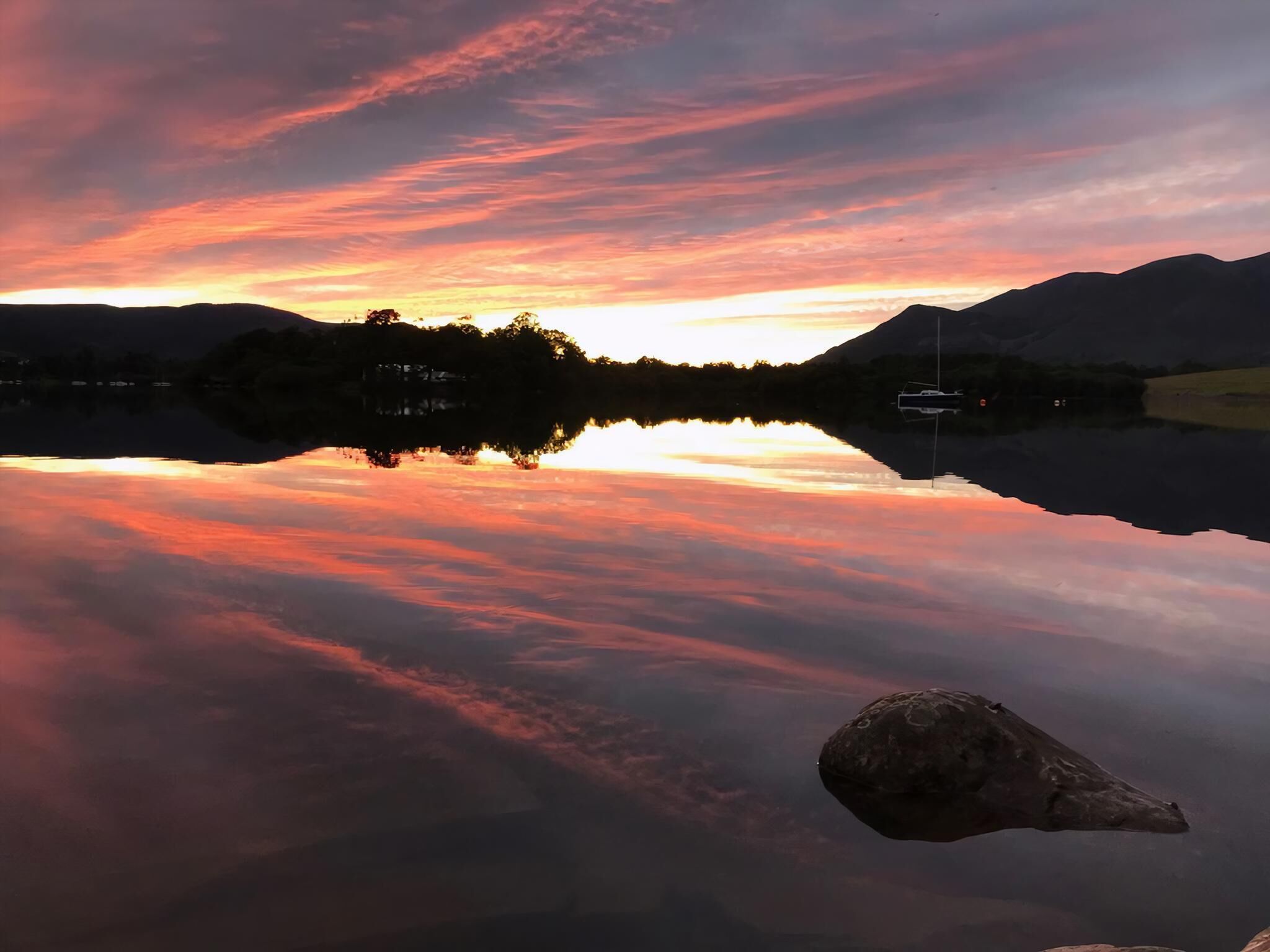 A calm lake reflecting a sunset with mountains in the background.