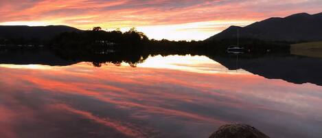 A calm lake reflecting a sunset with mountains in the background.